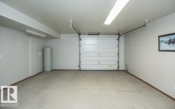 Attached garage featuring a white sectional door, concrete flooring, and ceiling-mounted fluorescent lighting - 