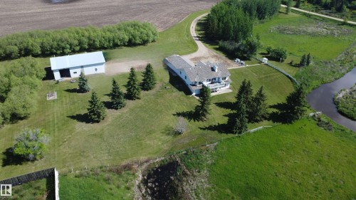 Expansive property featuring a white residence with multiple balconies, a detached barn, a winding driveway, mature evergreen trees, and a bordering waterway - 60230 Rg Rd 271, Rural Westlock County, AB 