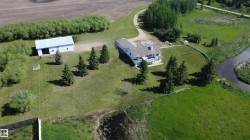 Expansive property featuring a white residence with multiple balconies, a detached barn, a winding driveway, mature evergreen trees, and a bordering waterway - 