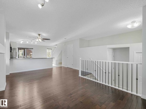 Spacious main living area featuring wide-plank wood-finish flooring, a contemporary ceiling fan, recessed lighting, a breakfast bar, and a staircase with metal balusters - 77 4050 Savaryn Drive, Edmonton, AB 