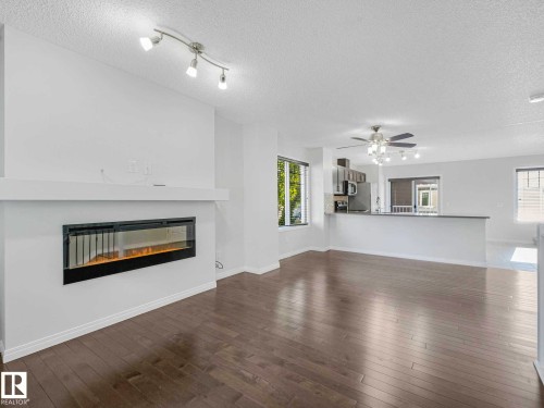 Open-concept living space featuring wood-finish flooring, a contemporary linear fireplace, and a kitchen with stainless steel appliances and a breakfast bar - 77 4050 Savaryn Drive, Edmonton, AB 