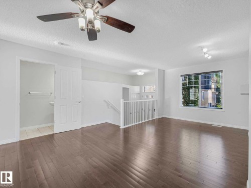 Spacious interior featuring wood-finish flooring, a ceiling fan with integrated lighting, and a large window with blinds - 77 4050 Savaryn Drive, Edmonton, AB 