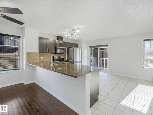 Open concept kitchen featuring dark wood cabinetry, stainless steel appliances, a breakfast bar, and a tile backsplash - 77 4050 Savaryn Drive, Edmonton, AB 