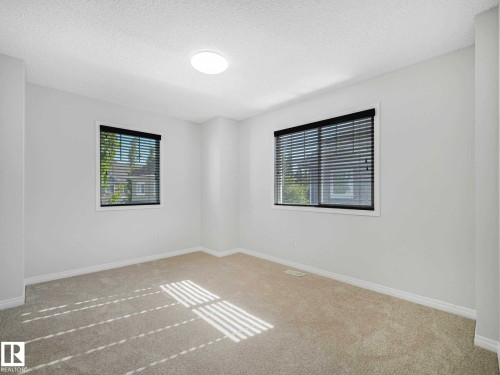 Carpeted interior space featuring two windows with horizontal blinds, a ceiling-mounted light fixture, and white baseboard trim - 77 4050 Savaryn Drive, Edmonton, AB 