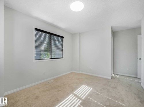 Carpeted room featuring a window with dark blinds, white baseboards, and a ceiling light fixture - 77 4050 Savaryn Drive, Edmonton, AB 
