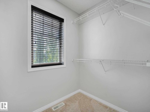 Walk-in closet featuring a window with blinds, white wire shelving, carpeting, white walls, and white baseboards - 77 4050 Savaryn Drive, Edmonton, AB 