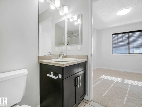 Vanity featuring an integrated sink, light-toned countertop, and dark wood-finish cabinetry - 77 4050 Savaryn Drive, Edmonton, AB 