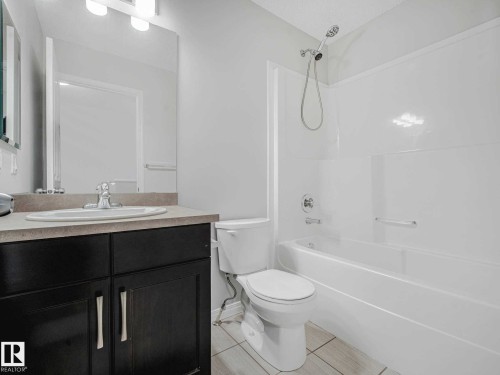 Bathroom featuring a white bathtub with a showerhead, a toilet, and a vanity with a rectangular sink - 77 4050 Savaryn Drive, Edmonton, AB 