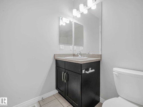 Bathroom featuring a dark wood-finish vanity with a light countertop, integrated sink, and an overhead vanity light fixture - 77 4050 Savaryn Drive, Edmonton, AB 