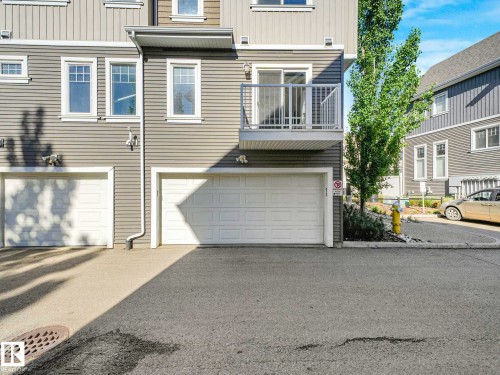 Exterior featuring horizontal siding, multiple windows, a second-story balcony with metal railings, and two integrated garage doors - 77 4050 Savaryn Drive, Edmonton, AB 