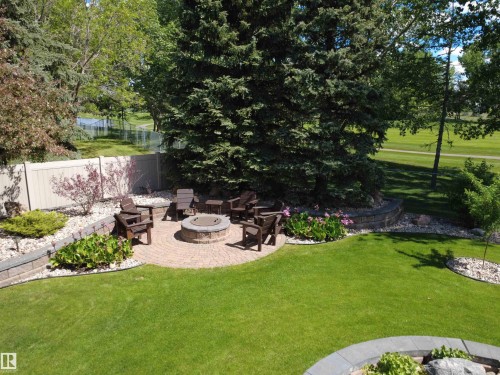 Circular paver patio featuring a built-in fire pit, surrounded by lush green lawn and mature trees - 915 Picard Drive Nw, Edmonton, AB 