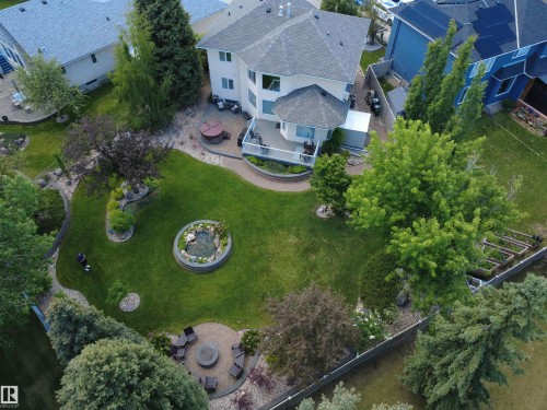 Expansive backyard featuring a manicured lawn, established landscaping, a circular fire pit area with paver stones, an elevated water feature, and a raised deck with a hot tub - 915 Picard Drive Nw, Edmonton, AB 