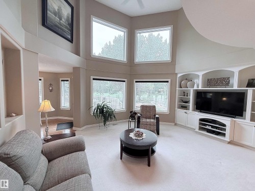 Living area featuring vaulted ceilings, built-in entertainment center with shelving and cabinetry, and multiple large windows - 915 Picard Drive Nw, Edmonton, AB 