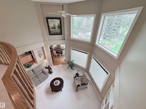 Two-story living area featuring a vaulted ceiling with a ceiling fan, a curved wooden staircase, and multiple large windows - 915 Picard Drive Nw, Edmonton, AB 