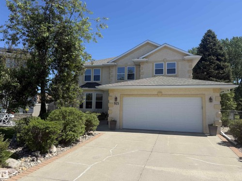 Two-story stucco residence featuring a dual garage door, concrete driveway with brick edging, and mature landscaping - 915 Picard Drive Nw, Edmonton, AB 