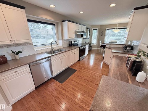Kitchen featuring white cabinetry, stainless steel appliances, wood-finish flooring, and ample natural light from multiple windows - 915 Picard Drive Nw, Edmonton, AB 