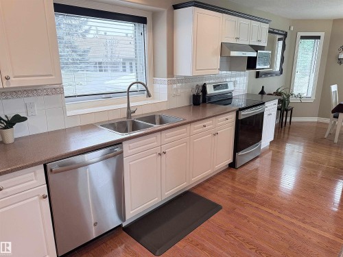 Kitchen featuring a dual basin sink, stainless steel appliances, light cabinetry with dark crown molding, and wood-finish flooring - 915 Picard Drive Nw, Edmonton, AB 