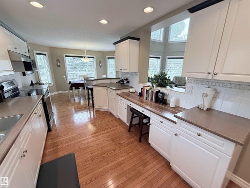 Spacious kitchen featuring wood-finish flooring, white cabinetry with silver hardware, and a built-in stainless steel range with overhead ventilation - 915 Picard Drive Nw, Edmonton, AB 