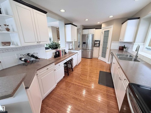Spacious kitchen featuring wood-finish flooring, white cabinetry with dark crown molding, and light-colored countertops - 915 Picard Drive Nw, Edmonton, AB 