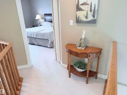 Carpeted hallway featuring wood stair railings, a neutral wall color, and white trim - 