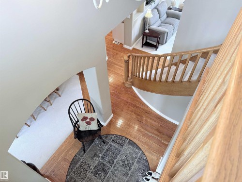 Expansive foyer featuring hardwood flooring, a circular area rug, and a curved staircase with natural wood banister and spindles - 915 Picard Drive Nw, Edmonton, AB 