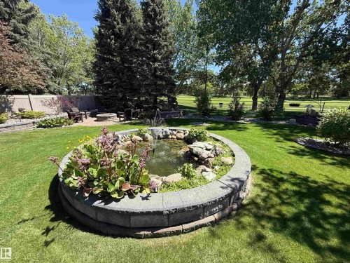 Landscaped backyard featuring a stone-lined pond with water feature, mature trees, a fire pit area, and a privacy fence - 915 Picard Drive Nw, Edmonton, AB 