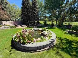 Landscaped backyard featuring a stone-lined pond with water feature, mature trees, a fire pit area, and a privacy fence - 