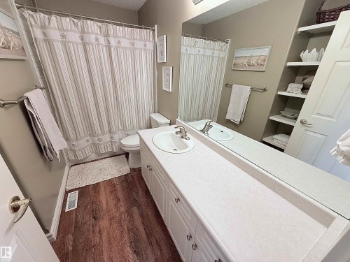Bathroom featuring a long vanity with a single basin, extensive mirror, wood-finish flooring, a toilet, and built-in shelving - 915 Picard Drive Nw, Edmonton, AB 