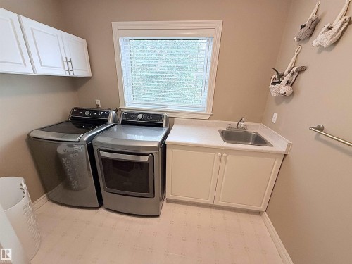 Laundry area with white upper cabinetry, a utility sink, and a window with blinds - 915 Picard Drive Nw, Edmonton, AB 