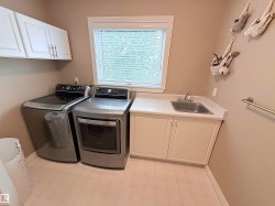 Laundry area with white upper cabinetry, a utility sink, and a window with blinds - 