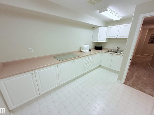 White cabinetry with a double basin sink, beige countertops, and patterned vinyl flooring - 915 Picard Drive Nw, Edmonton, AB 