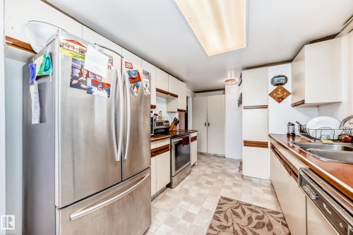 Kitchen featuring a stainless steel French door refrigerator, white cabinetry with wood-finish accents, and patterned tile flooring - 6804 102A Avenue, Edmonton, AB 