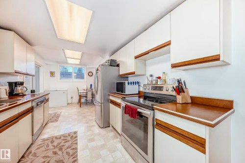 Galley kitchen featuring white cabinetry with wood accents, wood-finish countertops, and stainless steel appliances - 6804 102A Avenue, Edmonton, AB 