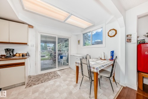 Kitchenette featuring white cabinetry with wood-finish accents, light-toned flooring, and a sliding glass door to the exterior - 6804 102A Avenue, Edmonton, AB 