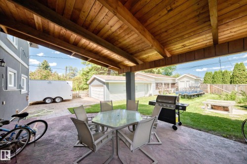 Covered patio with wood-finish ceiling, stamped concrete flooring, and an adjacent green space - 6804 102A Avenue, Edmonton, AB 