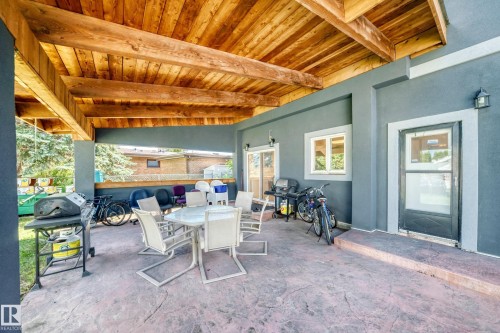 Covered outdoor patio featuring a wood-finish ceiling, stamped concrete flooring, and a sliding glass door - 6804 102A Avenue, Edmonton, AB 