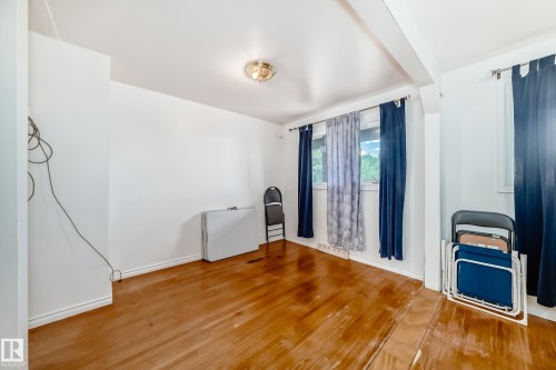 Spacious room featuring wood-finish flooring, white baseboards, and bright white walls - 6804 102A Avenue, Edmonton, AB 