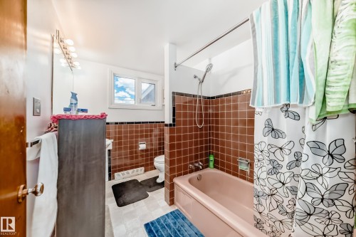 Bathroom featuring a built-in tub with shower, brown tiled walls, and a window for natural light - 6804 102A Avenue, Edmonton, AB 