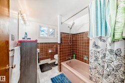 Bathroom featuring a built-in tub with shower, brown tiled walls, and a window for natural light - 