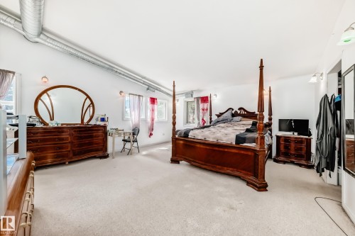 Carpeted bedroom featuring multiple windows, exposed metal ductwork, and wall-mounted light fixtures - 6804 102A Avenue, Edmonton, AB 