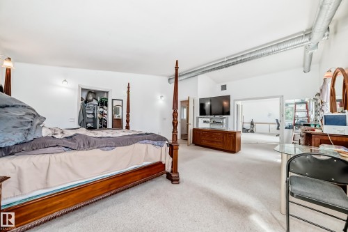Spacious room featuring vaulted ceilings, exposed ductwork, wall-mounted sconces, and light-colored carpeting - 6804 102A Avenue, Edmonton, AB 