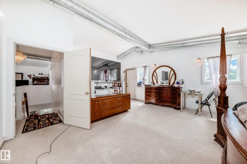 Spacious room featuring white walls, light-colored carpeting, two windows, exposed ductwork, and a built-in wood-finish media console - 6804 102A Avenue, Edmonton, AB 