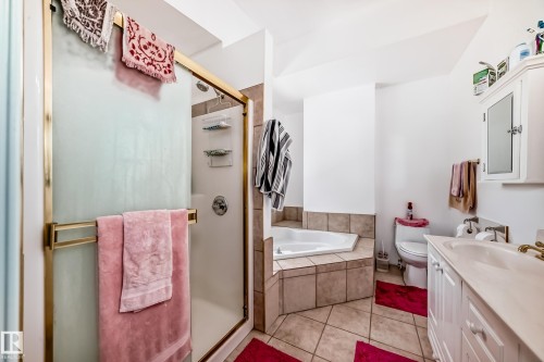 Bathroom featuring a corner soaking tub, tiled shower with gold-tone framed glass enclosure, a single vanity with storage, and a wall-mounted medicine cabinet - 6804 102A Avenue, Edmonton, AB 