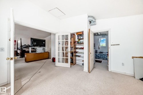 Carpeted room with white walls, featuring a French door closet with interior shelving and an open doorway to an additional room - 6804 102A Avenue, Edmonton, AB 