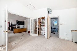 Carpeted room with white walls, featuring a French door closet with interior shelving and an open doorway to an additional room - 
