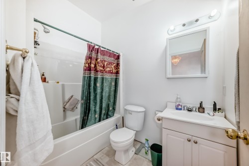 Bathroom featuring a white vanity with integrated sink, white tub/shower combination, and wall-mounted mirror with overhead lighting - 6804 102A Avenue, Edmonton, AB 