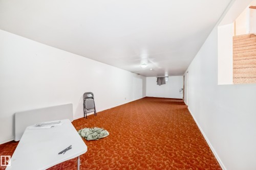 Spacious lower-level room featuring patterned orange carpeting, white painted walls, and overhead flush-mount lighting - 6804 102A Avenue, Edmonton, AB 