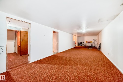 Spacious interior room featuring patterned carpeting, white painted walls, and a ceiling-mounted light fixture - 6804 102A Avenue, Edmonton, AB 