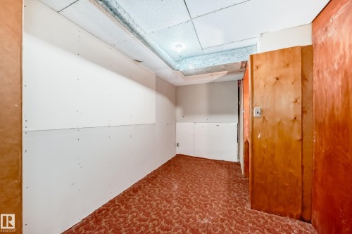 Unfinished interior space featuring exposed drywall, a drop ceiling, and patterned red flooring - 6804 102A Avenue, Edmonton, AB 