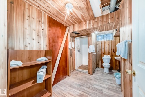 Wood-paneled room featuring a built-in shelving unit, white porcelain toilet, pedestal sink, and a shower area - 6804 102A Avenue, Edmonton, AB 